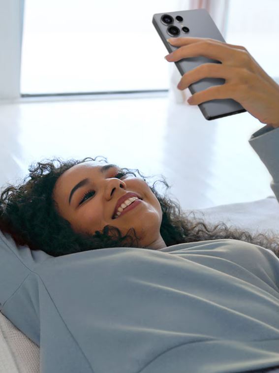 Μια γυναίκα είναι ξαπλωμένη και κρατάει ένα smartphone στο χέρι