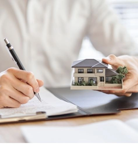 Ένα στυλό στο ένα χέρι και μια μακέτα ενός σπιτιού στο άλλο