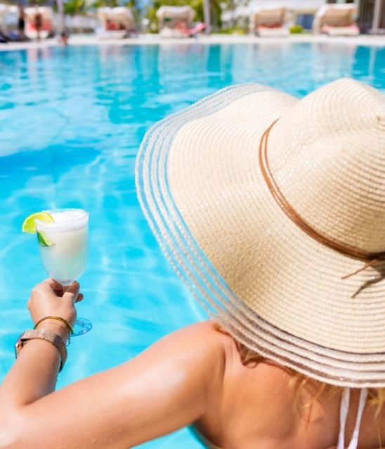 Μια γυναίκα με καπέλο σε μια πισίνα και ένα ποτό στο χέρι της